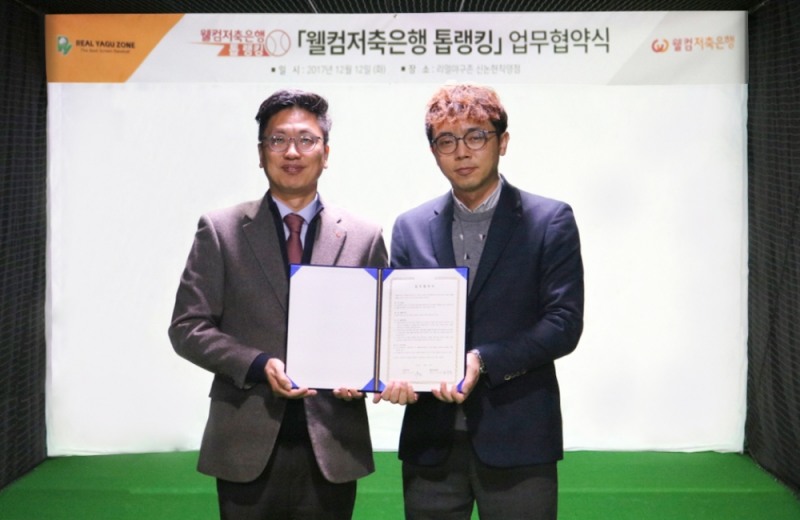 △김형태 웰컴금융그룹 전무와(왼쪽) 최윤태 리얼야구존의 가맹사업본부 본부장이 협약서를 들고 기념 촬영을 하고 있다./사진=웰컴저축은행