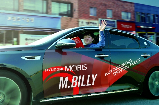 서산주행시험장 內 도로에서 자율주행차 M.BILLY를 테스트하는 연구원이 책을 보며 밖으로 손을 흔들고 있다. 사진=현대모비스.