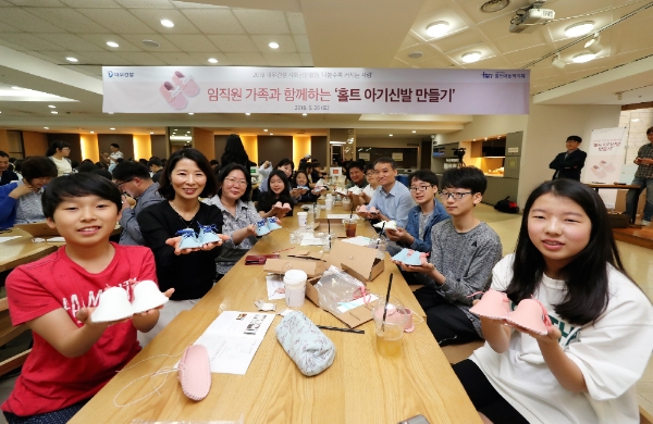 지난 26일 대우건설 본사에서 대우건설 임직원과 가족이 직접 만든 아기신발을 들고 포즈를 취하고 있다. / 사진=대우건설.