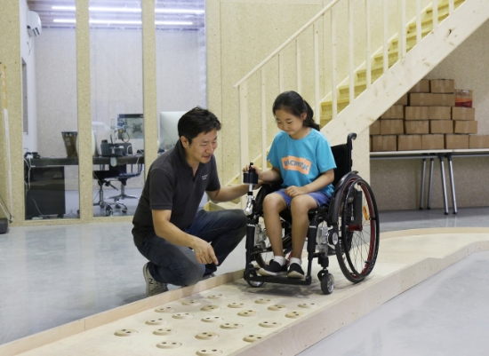 심재신 토도웍스 대표가 토도웍스 사옥에 위치한 휠체어 전용 교육장에서 장애 아동에게 수동휠체어용 전동 키트를 활용한 이동 교육을 진행하고 있다. 사진=SK행복나눔재단.