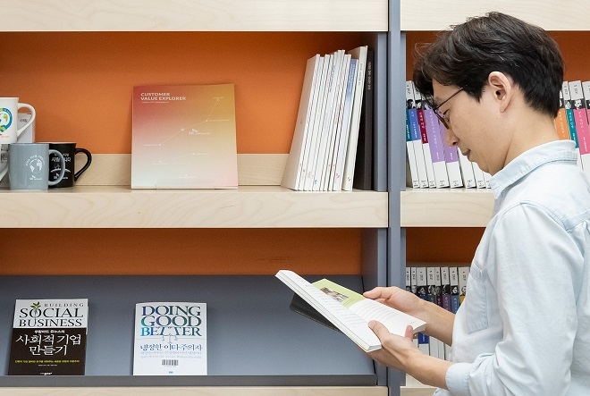 SK네트웍스 임직원이 새롭게 구성된 ‘사회적 가치’ 코너 앞에서 책을 읽고 있다. (사진=SK네트웍스)