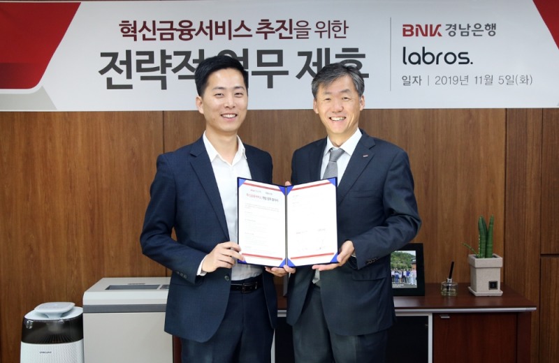 최우형 경남은행 부행장보(오른쪽)가 라브로스 주식회사 이창수 대표이사와 ‘모바일 외화 환전 혁신금융서비스 공동 개발 추진을 위한 업무 협약’을 체결하고 있다./사진=경남은행