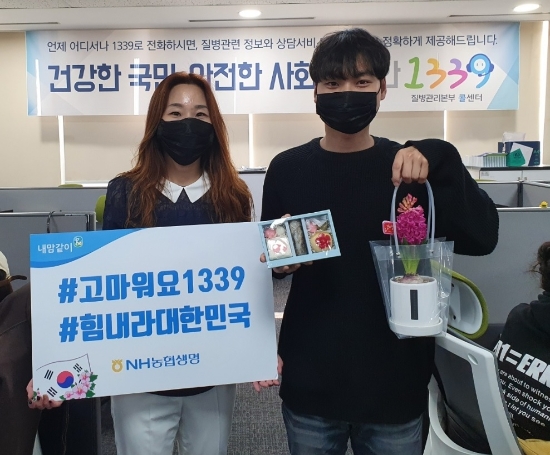 NH농협생명은 지난 13일 질병관리본부 1339 콜센터 직원에게 꽃 화분과 백설기 떡 300세트를 전달했다. 질병관리본부 1339 콜센터 센터장 박혜미(왼쪽)와 직원이 NH농협생명에서 보낸 꽃 화분과 떡을 들고 포즈를 취하고 있다. / 사진 = NH농협생명
