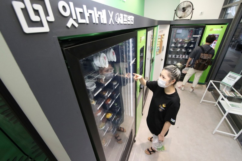 KT가 매장 관리형 에너지 최적화 상품인 ‘기가에너지 매니저 프랜차이즈 플러스’를 출시하고 ‘페이즈커뮤’의 무인점포들에 공급할 예정이라고 18일 밝혔다. KT 기가에너지 매니저 프랜차이즈 플러스가 적용된 서울 마곡나루의 ‘잇다가게’에서 고객들이 자판기를 이용해 비대면으로 반찬을 구매하고 있다./사진=KT