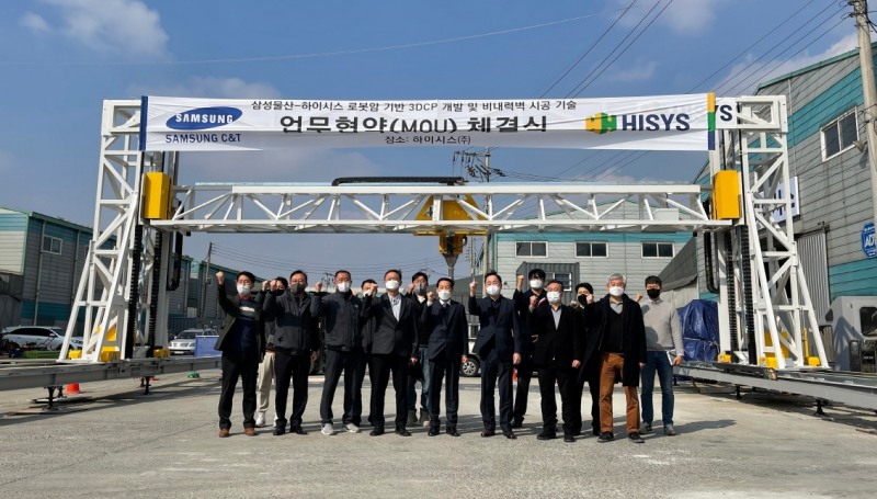 하이시스 정구섭 대표이사(오른쪽 7번째), 삼성물산 박성혁 상무(오른쪽 6번째) 등이 하이시스의 건축용 3D 프린터를 배경으로 협약식 체결 기념 촬영을 하고 있다. / 사진제공=하이시스