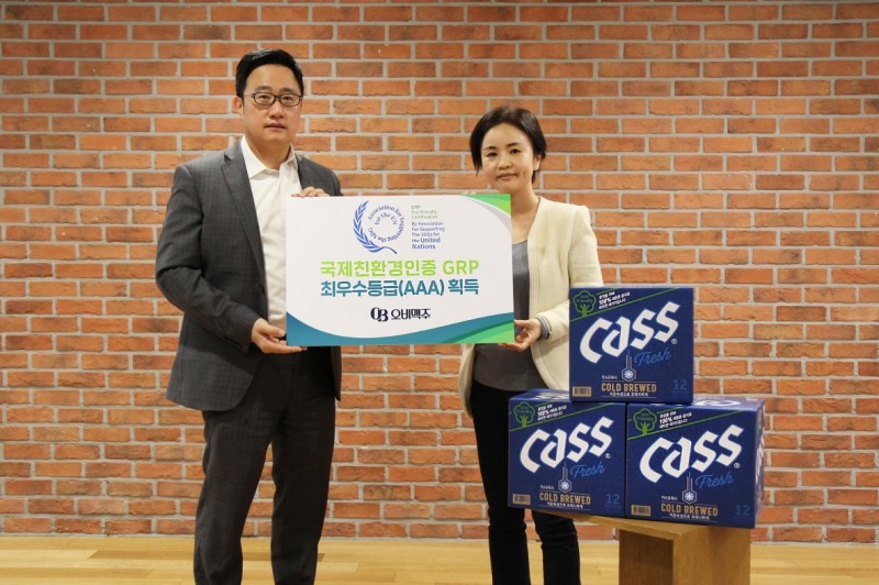 오비맥주 정책홍보부문 구자범 부사장(왼쪽)이 사회공헌팀 이은아 부장(오른쪽)과 함께 오비맥주 GRP 인증 최우수등급 획득을 기념해 100% 재생용지로 제작한 카스 병맥주 상자 앞에서 사진을 찍고 있다./ 사진제공 = 오비맥주