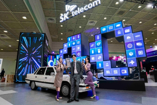 SKT의 WIS 2024 전시관 앞에서 가수 슬리피(가운데)와 모델들이 국내 최초의 무선전화 서비스 카폰(차량전화) 모형을 들고 포즈를 취했다. / 사진제공=SKT