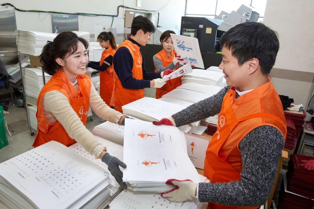 △한화봉사단 임직원들이 조판, 인쇄가 완료된 인쇄물을 검수한 후 재단과 타공을 하기 위해 옮기고 있다.