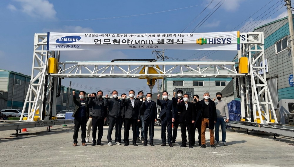 하이시스 정구섭 대표이사(오른쪽 7번째), 삼성물산 박성혁 상무(오른쪽 6번째) 등이 하이시스의 건축용 3D 프린터를 배경으로 협약식 체결 기념 촬영을 하고 있다. / 사진제공=하이시스