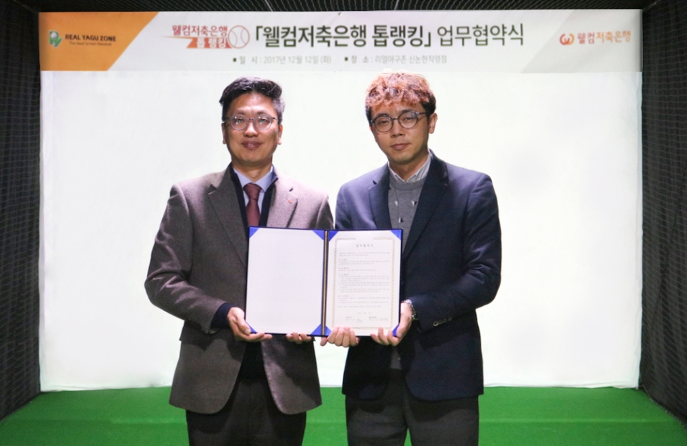 △김형태 웰컴금융그룹 전무와(왼쪽) 최윤태 리얼야구존의 가맹사업본부 본부장이 협약서를 들고 기념 촬영을 하고 있다./사진=웰컴저축은행