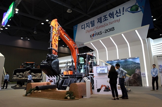 두산인프라코어가 ‘2018 국제자동화정밀기기전’에서 처음 선보이는 굴삭기용 스마트 솔루션 ‘두산 머신 가이던스’ 시스템을 관람객들이 둘러보고 있다.