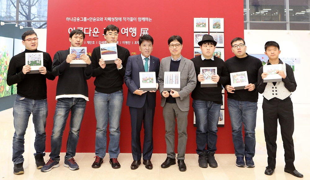 하나금융그룹은 3일 오전 을지로 KEB하나은행 신사옥 로비에서 2019년 하나금융그룹 캘린더 작품의 작가인 안윤모와 자폐성 장애작가 5인의 작품 전시회를 개최했다. 함영주 KEB하나은행장(사진 왼쪽에서 네 번째)이 캘린더에 실린 본인의 작품을 든 안윤모 작가 및 자폐성 장애작가들과 기념사진 촬영을 하고 있다. 사진 왼쪽부터 이병찬 작가, 김태영 작가, 조재현 작가, 함영주 행장, 안윤모 작가, 계인호 작가, 김세중 작가, 자폐성 장애 하프 연주자 안용주. / 사진= KEB하나은행
