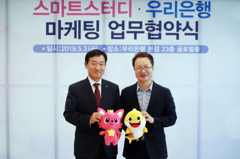 정채봉(사진 왼쪽) 우리은행 영업부문장과 이승규 스마트스터디 CFO 가 핑크퐁과 아기상어 인형을 들고 기념사진 촬영을 하고 있다./사진=우리은행