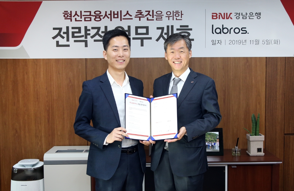 최우형 경남은행 부행장보(오른쪽)가 라브로스 주식회사 이창수 대표이사와 ‘모바일 외화 환전 혁신금융서비스 공동 개발 추진을 위한 업무 협약’을 체결하고 있다./사진=경남은행